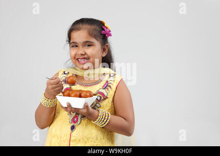 Girl eating Jamun Gulab and smiling Banque D'Images