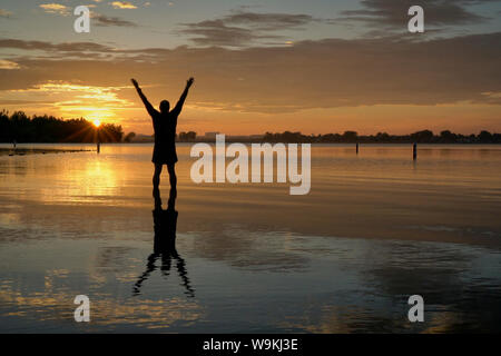 Lever du soleil silhouette d'un homme debout dans l'eau peu profonde et l'étirement ou la pratique de mouvements chigong, Boyd Lake State Park dans le nord du Colorado Banque D'Images