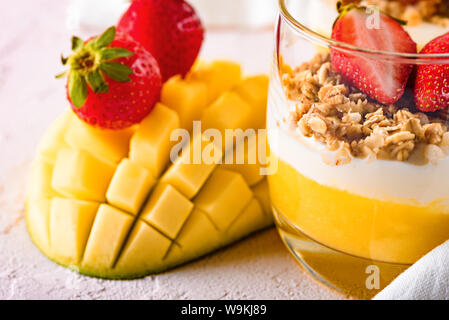 Gros plan du dessert à la mangue, mousse de lait caillé, granola et fraises sur fond rose clair. concept de petit-déjeuner sain et savoureux Banque D'Images