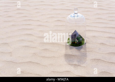 Maison en carton jouet avec pelouse verte protégée par un dôme en verre cloche parmi d'un désert de sable sans vie Banque D'Images