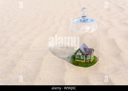 Maison en carton jouet avec pelouse verte protégée par un dôme en verre cloche parmi d'un désert de sable sans vie Banque D'Images