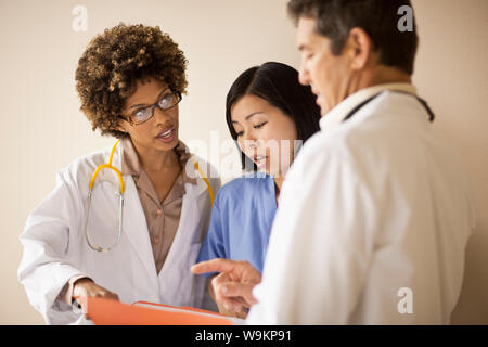 Trois médecins de discuter des dossiers de patient dans un couloir. Banque D'Images