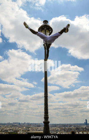 Artiste de rue à Paris, France, l'exécution sur un lampadaire à Sacré-Cœur sur la ville. Aptitudes de football et acrobatiques athlétisme. Skyline Banque D'Images