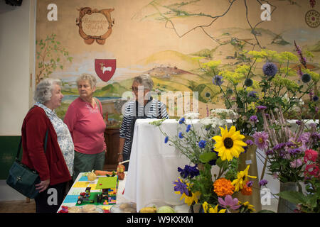 Spectacle de fleurs de village des années 2010 UK. Dames âgées, femmes à un événement communautaire. La murale sur le mur de la salle du village est de leur communauté dans les collines Brendon, Exmoor. Le bouclier l'écusson de la famille Ralph. Brompton Ralph, Somerset, West Country, Angleterre 10 août 2019 HOMER SYKES Banque D'Images