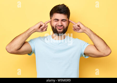A souligné l'homme nerveux temples de massage pour soulager la douleur, guy souffrant de maux de tête Migraine isolé sur fond jaune. homme essayant de se concentrer Banque D'Images