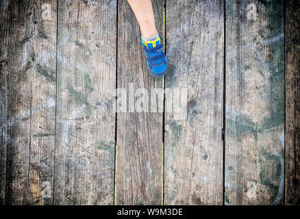 Le pied d'enfants sur la vieille planche de bois usé-de-chaussée. Les enfants porte des sneakers bleu. Marbre est vert, pelée couleurs. Gravé avec divers amour et autres inscri Banque D'Images