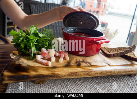 Jeune femme a les mains ouvertes bortsch pot couvercle. Soupe de betteraves traditionnelle russe. Matières et végétalien avec tomates, pommes de terre, le lard, la crème, le persil, garli Banque D'Images