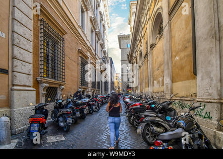 Une femme marche seul dans une petite rue latérale, avec beaucoup de motos en stationnement sur un côté ou dans le centre historique de Rome, Italie Banque D'Images