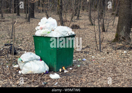 Vieux conteneur à ordures vert en métal rouillé plein de déchets en plastique dans le parc de la ville ou la forêt. Pollution de l'environnement Banque D'Images