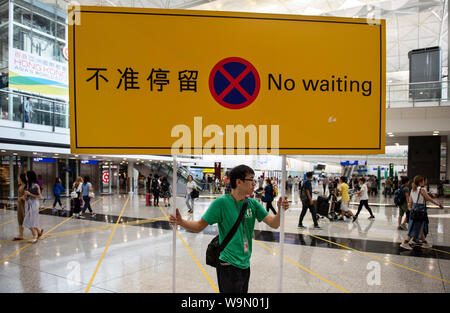 Un travailleur de l'aéroport porte un signe qui indique 'pas d'attente" à l'aéroport international de Hong Kong : le hall d'arrivée.Le fonctionnement de l'aéroport international de Hong Kong a reprendre en grande partie de la normale que l'administration aéroportuaire a obtenu une injonction provisoire de s'abstenir des gens de manière illégale et obstruction délibérée ou interférer avec l'utilisation appropriée de l'aéroport après une nuit chaotique de protestation dans laquelle les manifestants du passager bloqué l'accès à l'embarquement causant des centaines de vols annulés. Banque D'Images