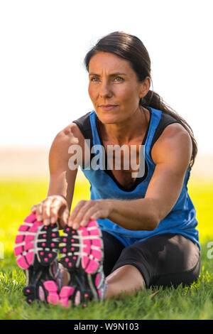 Young caucasian woman s'étend, médite, et se concentre dans l'herbe à l'extérieur dans un parc Banque D'Images