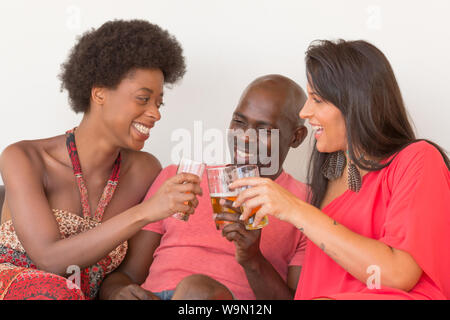 Trois amis multiculturels, rire et parler sur la table avec les boissons alcoolisées lors d'une partie de la chambre ou rassemblement Banque D'Images