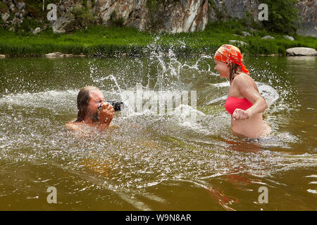 Homme mature humide avec appareil photo numérique dans les mains et très jolie femme jouent dans la rivière. Banque D'Images