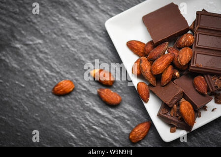 Barre de chocolat aux amandes écrou sur plaque blanche sur le fond sombre / morceaux dessert sucré Bonbons et collations Banque D'Images