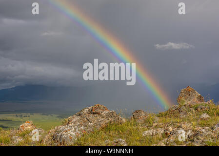 Arc-en-ciel lumineux incroyable close-up sur les montagnes et d'une vallée contre un ciel d'orage avec pluie et nuage et rochers en premier plan Banque D'Images