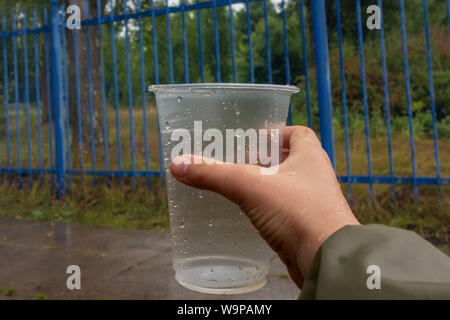 Verre avec des gouttelettes d'eau en main pour enfants. Garçon recueille des gouttes de pluie à l'extérieur. Concept de l'eau douce et pure, style de vie actif et de parent. L'écologie et du Banque D'Images