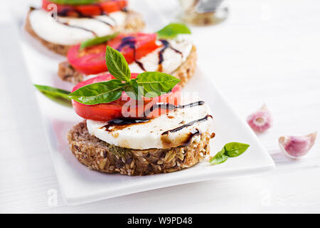 Des sandwichs avec de la mozzarella, tomates et pain de seigle sur table en bois blanc. Banque D'Images
