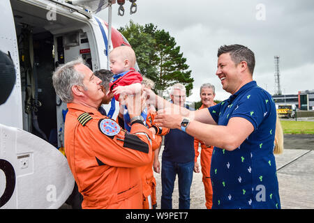 De 0001 SOUS EMBARGO VENDREDI 16 AOÛT HM Coastguard Chef d'équipage Ian Copley ascenseurs one-year-old Jenson Powell de son père riche Powell car ils rencontrent pour la première fois en un an que lui et son équipage évacué des garde-côtes HM sa femme Jennie (caché dans pic) par hélicoptère à Oxford de Cornouailles après Jennie entre en travail à 22 semaines avec ses jumeaux, l'accouchement le plus jeune avant terme survivant des jumeaux nés en Grande-Bretagne. Banque D'Images