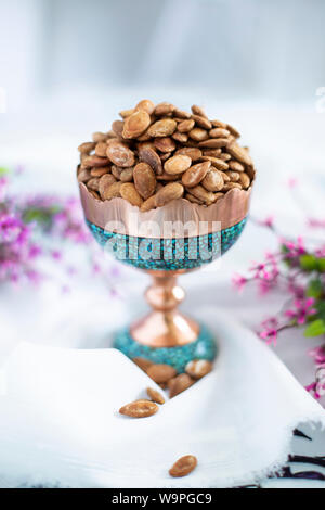 Un bol de graines de citrouille rôties dans un plat traditionnel turquoise et cuivre, garni de fleurs Banque D'Images