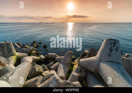 Magnifique coucher de soleil paysage marin. Les brise-lames de la jetée à terre les tétrapodes. Navires de fret à l'horizon. Rêves de voyages et de motivation Banque D'Images