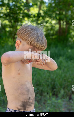 Contrariée, triste et pleurant caucasian boy 5 ans avec des cheveux blonds, taché ou sale. Se frotte les yeux. À l'extérieur Banque D'Images