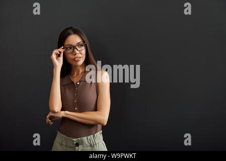 Smart et les jeunes. Asian businesswoman adjusting eyeglasses et à côté en se tenant debout sur un fond sombre. Les gens d'affaires. Concept de travail Banque D'Images