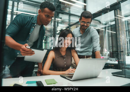 Les gens d'affaires. Groupe de trois jeunes et joyeux employés utilisant les technologies modernes tout en travaillant dans un bureau moderne. Concept d'emploi. Lieu de travail Banque D'Images