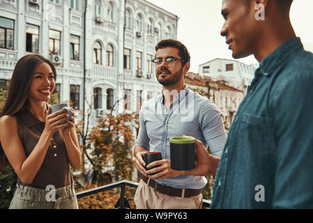 Se détendre après le travail. Les jeunes collègues positifs dans des vêtements décontractés holding tasses et discuter de quelque chose en étant debout sur le balcon. Les collègues à se reposer. Pause café Banque D'Images