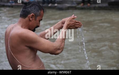 Katmandou, Népal. Août 15, 2019. Un homme propose des prières avec de l'eau bénite pendant la Janai Purnima festival au temple de Pashupatinath à Katmandou, Népal, le 15 août, 2019. Pendant ce festival, les Hindous prendre bain saint et effectuer le changement annuel de la Janai, une chaîne de coton sacré porte autour de la poitrine ou attaché au poignet, dans la conviction qu'il n'accordera de protection et les purifier. Credit : Sunil Sharma/Xinhua Banque D'Images