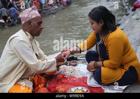 Katmandou, Népal. Août 15, 2019. Un prêtre un fil sacré des liens à une femme pendant l'Janai Purnima festival au temple de Pashupatinath à Katmandou, Népal, le 15 août, 2019. Pendant ce festival, les Hindous prendre bain saint et effectuer le changement annuel de la Janai, une chaîne de coton sacré porte autour de la poitrine ou attaché au poignet, dans la conviction qu'il n'accordera de protection et les purifier. Credit : Sunil Sharma/Xinhua Banque D'Images