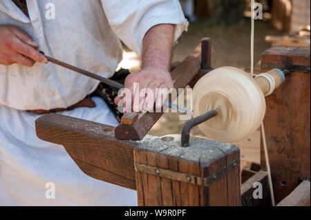Un artisan sculpte un morceau de bois à l'aide d'une ancienne tour, conduit avec pédale. Banque D'Images