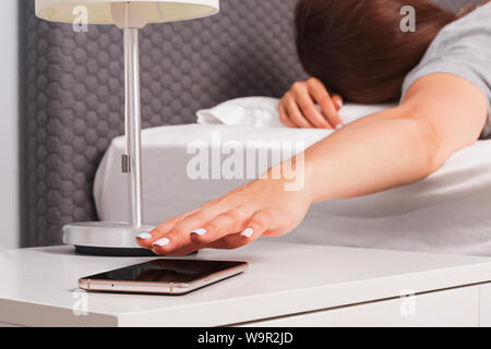 Close-up shot of woman's hand essayant de rejoindre sonnerie du téléphone posé sur la table de nuit d'avoir certains répéter tôt le matin. Banque D'Images