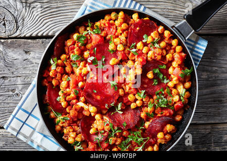 Close-up de chiche fritos, poêlée de pois chiches au chorizo, jambon, tomates et épices dans une poêle, vue horizontale à partir de ci-dessus, flatlay Banque D'Images