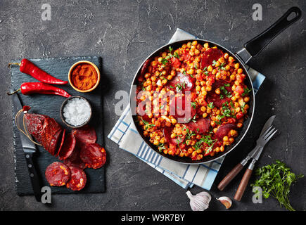 Chiches pois chiches frits avec fritos, chorizo, tomates jambon et les épices dans une poêle sur une table en béton avec des ingrédients de spécialités espagnoles, horizontal Banque D'Images