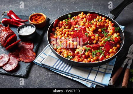 Close-up de chiche fritos, poêlée de pois chiches au chorizo, jambon, tomates et épices dans une poêle sur une table en béton avec des ingrédients, la cuisine espagnole Banque D'Images