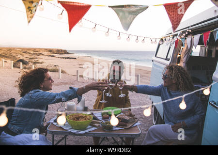 Happy friends clameurs et de boire du vin au cours de vacances camping à la plage avec vintage van. Les gens s'amuser à week-end soir d'été avec campe Banque D'Images