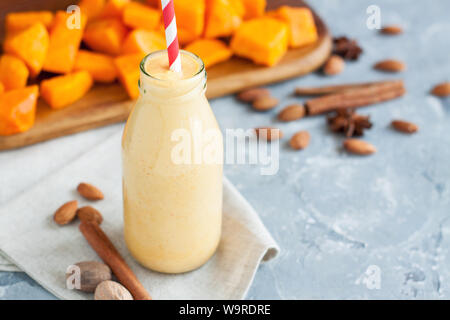 Petite bouteille remplie d'orange et d'amande smoothie santé avec paille rouge tourbillonnait avec des tranches de citrouille et épices sur fond gris Banque D'Images