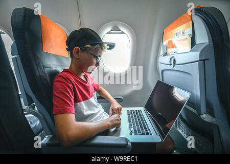 Beau Garçon jouant avec un ordinateur portable lors des déplacements en avion. Les jeunes blogger partager voyage en ligne vidéo social travaillant avec des adolescents au cours de l'ordinateur fly Banque D'Images