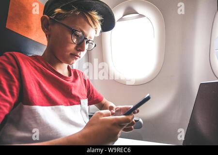 Beau Garçon jouant avec le smartphone lors des déplacements en avion. Les jeunes billet blogger partager vidéo social sur la ligne de jouer avec de l'adolescence au cours de téléphone cellulaire Banque D'Images