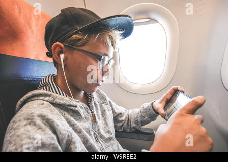 Beau Garçon jouant avec le smartphone lors des déplacements en avion. Les jeunes billet blogger partager vidéo social sur la ligne de jouer avec de l'adolescence au cours de téléphone cellulaire Banque D'Images