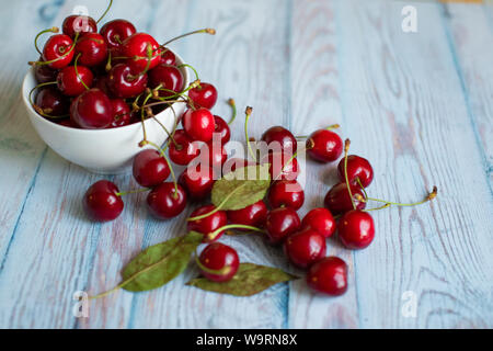 Cerises rouges frais dans une assiette blanche sur un fond bleu clair, de l'espace pour texte, concept de la nourriture végétarienne douce naturelle Banque D'Images