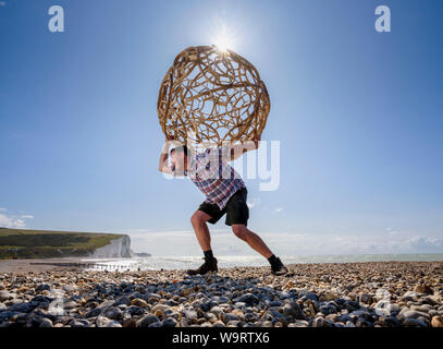 Cuckmere Haven, au Royaume-Uni. 15 août, 2019. Artiste Keith Pettit place le premier d'une série de machine à vapeur-bent chestnut sphères sur la plage de Cuckmere Haven dans l'East Sussex. Faites en collaboration avec trug bouilloire Charlie Groves, les formes complexes sont inspirés par les ossements de coccolithes ancienne - le carbonate de calcium reste qui composent la craie des South Downs. L'exposition 'What Lies Beneath' sera à l'emblématique coastguard cottages donnant sur les falaises des sept Sœurs (photo). Crédit : Jim Holden/Alamy Live News Banque D'Images