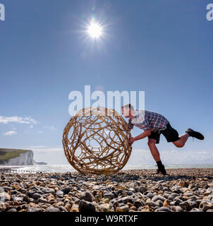 Cuckmere Haven, au Royaume-Uni. 15 août, 2019. Artiste Keith Pettit place le premier d'une série de machine à vapeur-bent chestnut sphères sur la plage de Cuckmere Haven dans l'East Sussex. Faites en collaboration avec trug bouilloire Charlie Groves, les formes complexes sont inspirés par les ossements de coccolithes ancienne - le carbonate de calcium reste qui composent la craie des South Downs. L'exposition 'What Lies Beneath' sera à l'emblématique coastguard cottages donnant sur les falaises des sept Sœurs (photo). Crédit : Jim Holden/Alamy Live News Banque D'Images