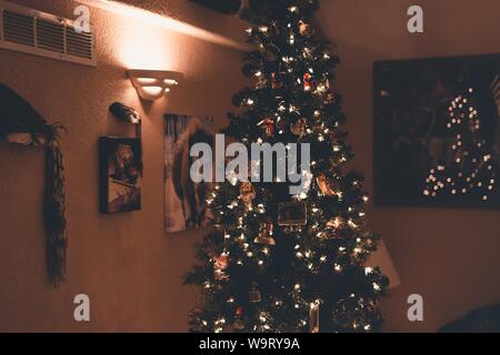 Belle photo d'un arbre de Noël avec ornements et lumières près des photos et des cadres sur un mur Banque D'Images