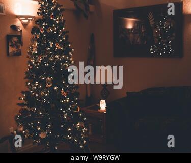 Belle photo d'un arbre de Noël avec ornements et lumières près des photos et des cadres sur un mur Banque D'Images