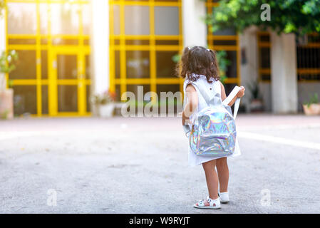 Retour à l'école. Cute child girl avec sac à dos holographique en marche et aller à l'école avec plaisir.dos, vue arrière d'un tout-petit enfant à marcher en direction de l'éducation préscolaire avec la porte à l'arrière-plan. Banque D'Images