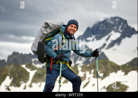 Hiker homme se sur la falaise contre le sommet d'une montagne. L'homme a un sac à dos et bâtons de marche. Les randonnées en montagne. Copy space Banque D'Images