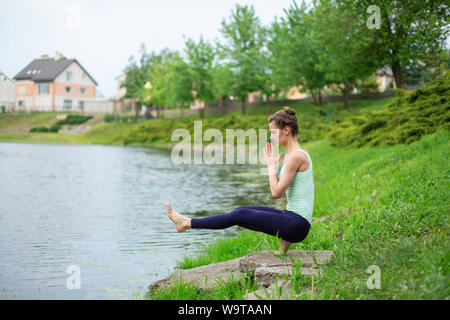 Jeune fille brune mince yogi ne difficile les exercices de yoga sur l'herbe verte sur le fond de l'eau. Banque D'Images