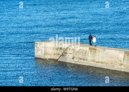 Tynemouth, England, UK - 4 Février 2019 : un couple à pied le long du brise-lames du port de Cullercoats sur la côte de la mer du Nord de Tyneside. Banque D'Images