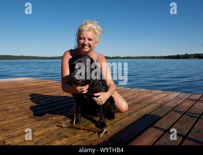 Femme assise sur une jetée en bois d'un labrador noir serrant, Lituanie Banque D'Images